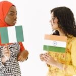 Two women celebrate diversity by holding Nigerian and Indian flags, symbolizing unity and friendship.