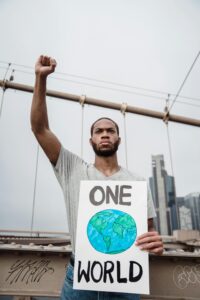A man raising a fist and holding a 'One World' placard during an outdoor protest.