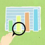 Top view of decorative cardboard illustration of hand with magnifying glass above diagram with columns on green background