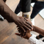 Diverse hands uniting in teamwork inside a professional office environment.